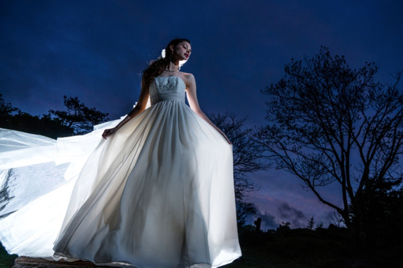 Example image of a woman in a white dress at night with trees in the background